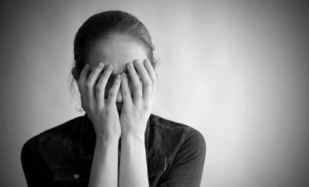 A black and white image of a woman covering her face, representing stress and anxiety, with a focus on mental health issues and the need for professional support.