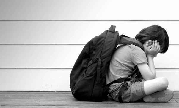 A young child sitting on the floor with a backpack, appearing upset, representing issues related to education or emotional wellbeing in children.