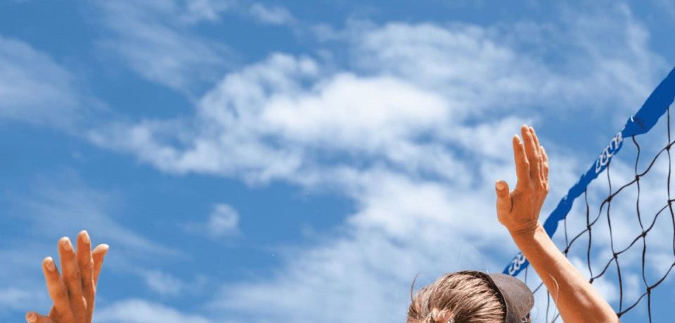 A female volleyball player jumping to hit the ball over the net against a bright blue sky, showcasing athleticism and empowerment for legal and business success.