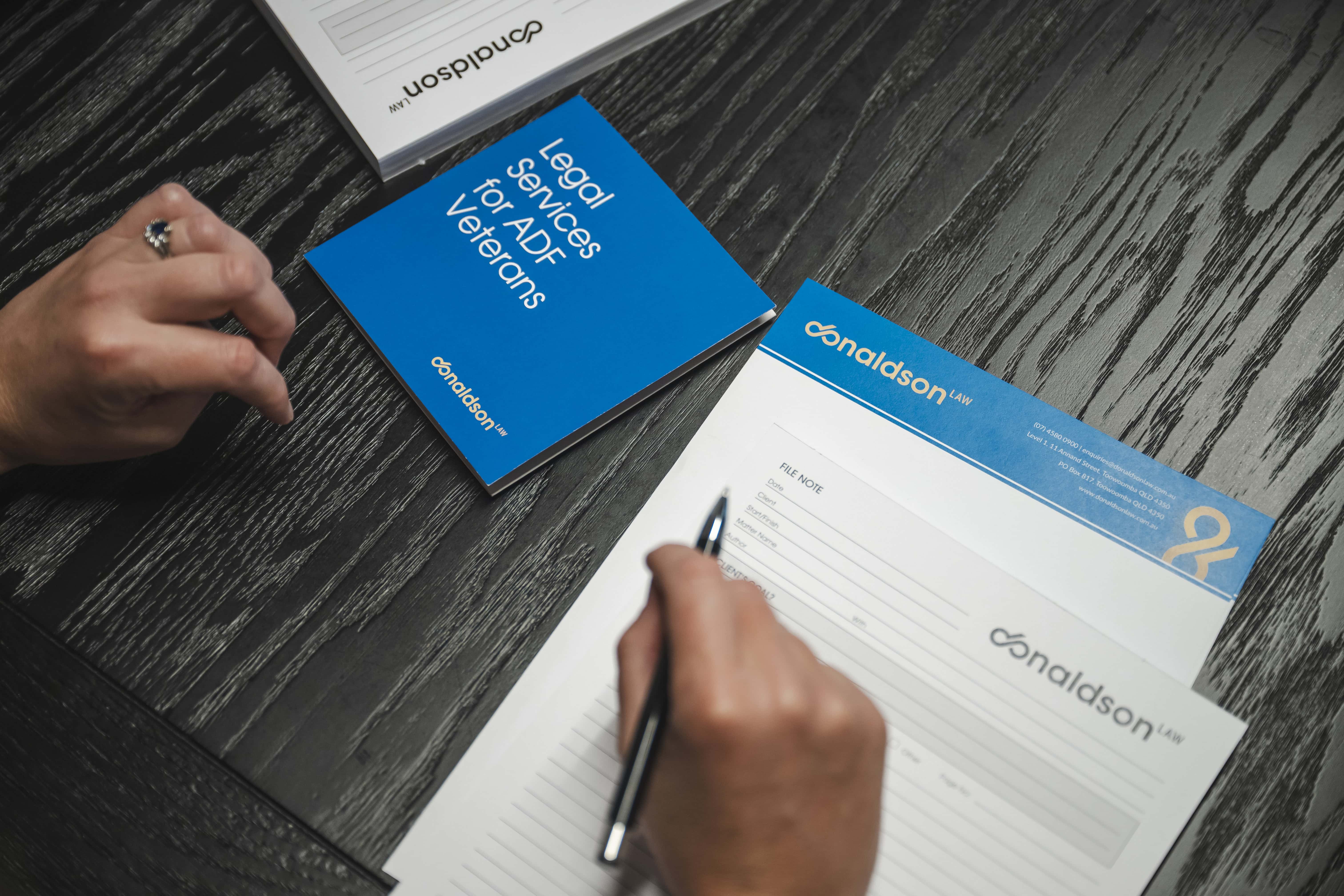 A person reviewing legal documents and brochures from a law firm specialising in legal services for ADF veterans, offering expert legal assistance and advice.